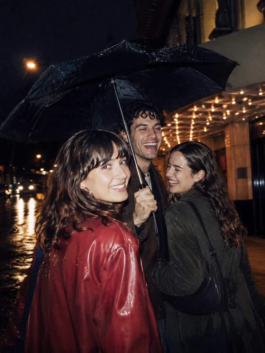 Three friends laughing beneath an umbrella after a late movie, photographed with Tumble's Flash Night film look.